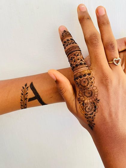 A combination of two minimalist designs: a single detailed finger and a custom initial on the wrist.