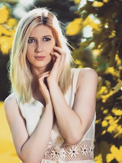 A close-up portrait where the bright yellow and green foliage provides a vibrant, natural backdrop. The focus is on the model's expression, captured with soft light to create a gentle and engaging look.