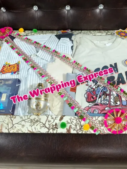 Holi trousseau packing that includes new clothes for the family, a silver 'pichkari', and a gold bar, all decorated with colorful gota patti lace.