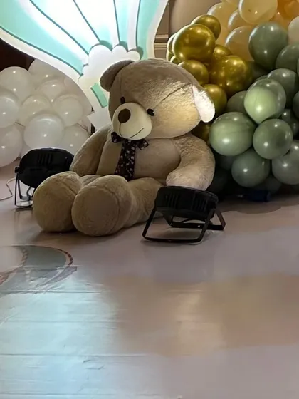 A large, soft teddy bear prop sits among the balloon decorations, adding a cuddly and inviting element to the party decor.