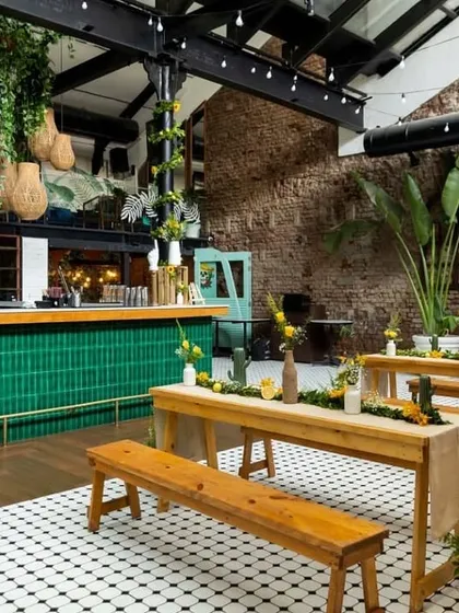 A wide view of the decor at Cafe Panama, showing the contrast between the emerald green bar, the rustic wooden furniture, and the industrial brick walls. The hanging cane lamps add a touch of warmth.