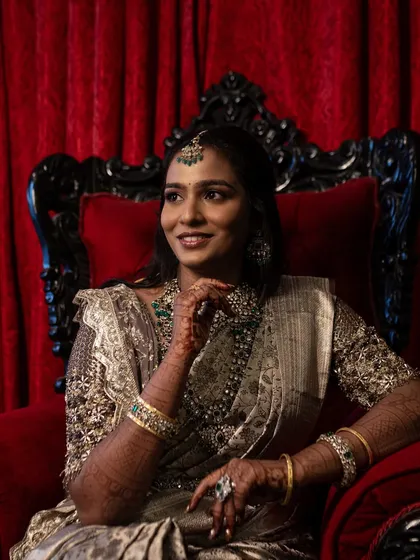 Sruthi looking regal and elegant, seated on a red throne chair. Her makeup and elaborate jewellery create a look of timeless sophistication.