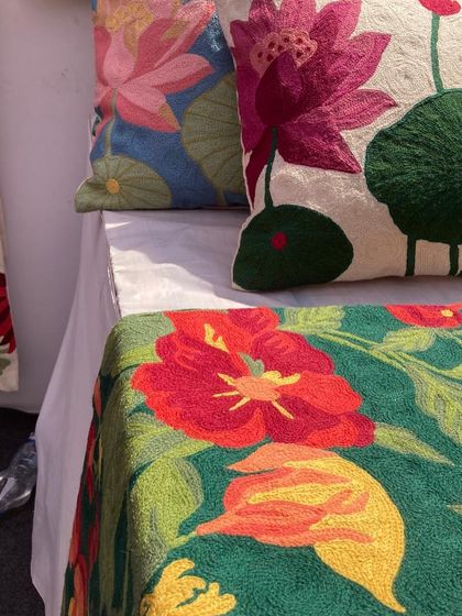A vibrant collection of hand-embroidered cushion covers and a bedspread, featuring bold floral and lotus motifs.