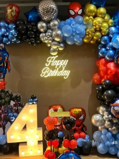 An action-packed superhero birthday setup for a 4-year-old. It features a balloon arch with foils of Superman, Iron Man, and Spider-Man, plus a large light-up number '4'.