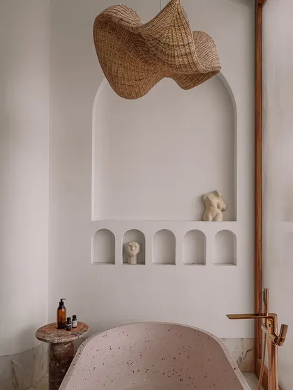 This moody, Billie Eilish-inspired bathroom features a large, freestanding terrazzo bathtub. The space is designed for atmosphere, with arched niches for art and a dramatic woven pendant light, creating a sanctuary for relaxation and creative thought.
