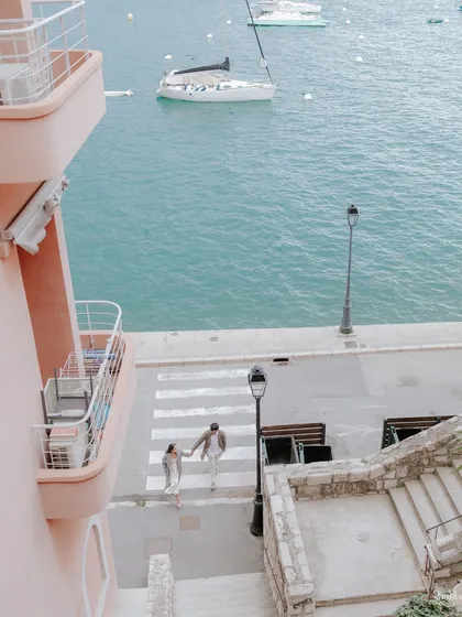An aerial view of the couple walking hand-in-hand by the harbor in Nice, capturing the picturesque beauty of the French Riviera.