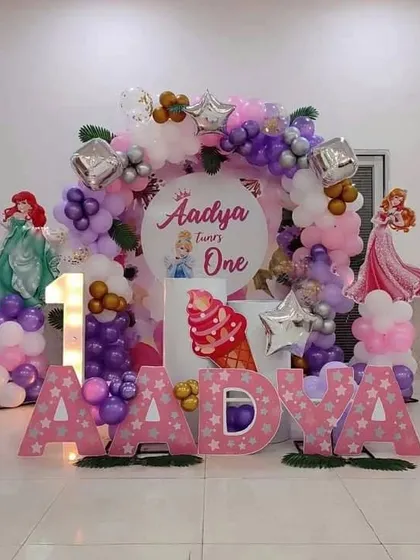 A magical Disney Princess first birthday theme for Aadya. This decoration features character cutouts of Ariel and other princesses, a personalized backdrop, marquee letters, and a light-up number '1'.