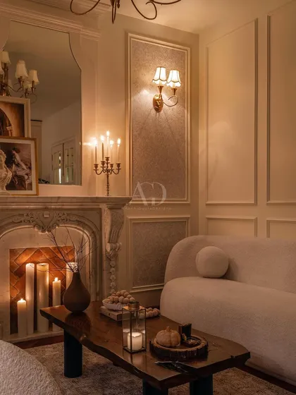A beautifully composed shot of the fireplace area, where the mirror reflects the room's chandelier and adds depth. The arrangement of furniture and decor feels both deliberate and effortlessly elegant.