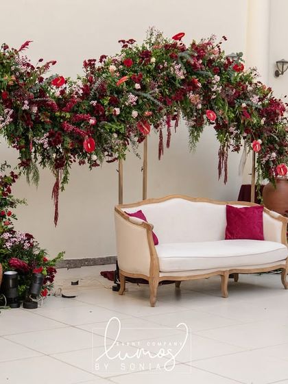 A beautiful floral arch in rich red hues serves as the backdrop for this elegant reception stage. The classic white sofa and terracotta pots add a touch of rustic charm.