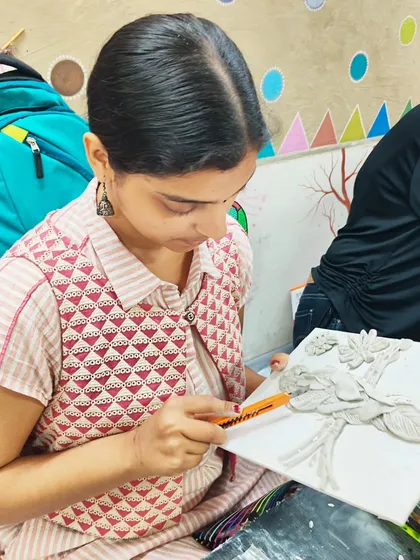 A student using a craft knife to carve fine details into her clay relief artwork, a technique for achieving precision in sculptural pieces.