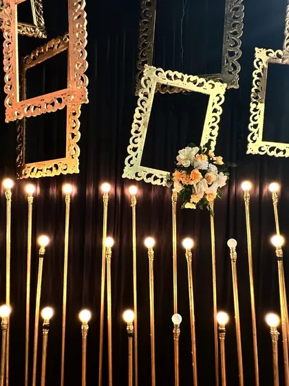 A photo corner that is all about moody glamour. Golden frames hang against a dark backdrop, illuminated by a field of warm bulb lights, creating an artistic and dramatic setting.