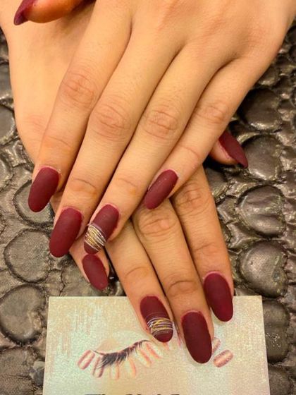 A sophisticated set of long, almond-shaped nails in a deep, matte red. The ring fingers are accented with a subtle, multi-colored thread design.