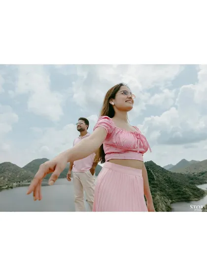 A creative shot of the bride-to-be reaching towards the camera, with the stunning lake and mountains of Udaipur behind her.