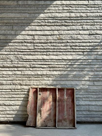 A piece of wooden formwork leaning against a newly completed section of stone wall, a poetic image of the construction process.