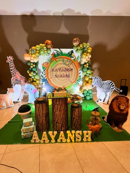A wild jungle safari adventure for Aayansh's birthday. The scene is set with lifelike animal cutouts including a lion, zebra, and giraffe, alongside log-themed plinths and a lush green floor mat to create an immersive safari experience.