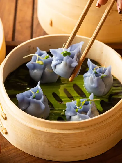 A close-up of a blue dumpling being held by chopsticks, showcasing the texture and color.