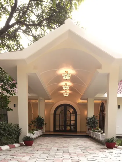 A closer view of the Doon Homestay's entrance portico. The design balances architectural form with soft landscaping, using potted plants and low hedges to soften the lines and guide visitors toward the arched doorway.