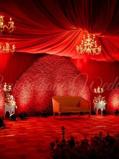 A bold and dramatic all-red reception stage. The textured floral backdrop, draped ceiling, and chandeliers create a look of pure royal opulence.