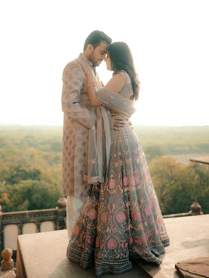A romantic portrait of a couple overlooking a lush green valley from a stone balcony. The soft, golden hour light adds a dreamy quality to this elegant pre-wedding photograph.