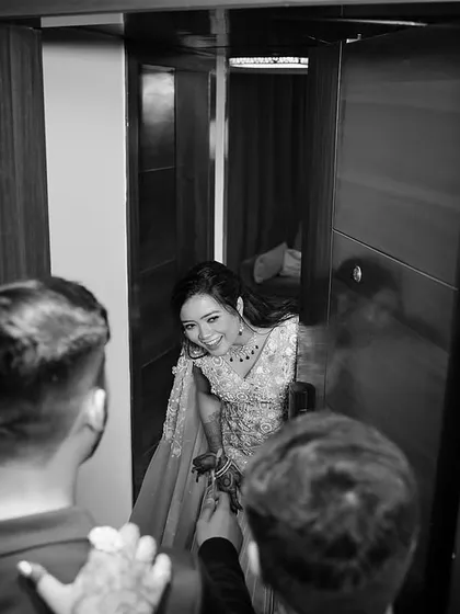 A candid moment captured in monochrome. The bride peeks out from a doorway with a joyful laugh, and the black and white treatment emphasizes the raw emotion and happiness of the moment.
