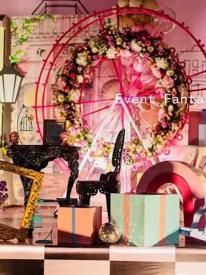 A chic and elegant Parisian-themed party for Manogna's first birthday. The setup features a sketch-style backdrop of Parisian streets, a floral-covered Ferris wheel, and vintage props like lanterns and suitcases.