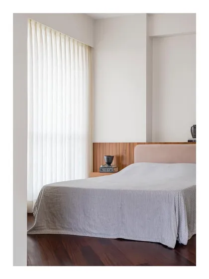 A bedroom designed for restraint and calm. The custom bed features a simple, low headboard in a soft, neutral fabric, set against a dark wood floor to create a space that lets you breathe.