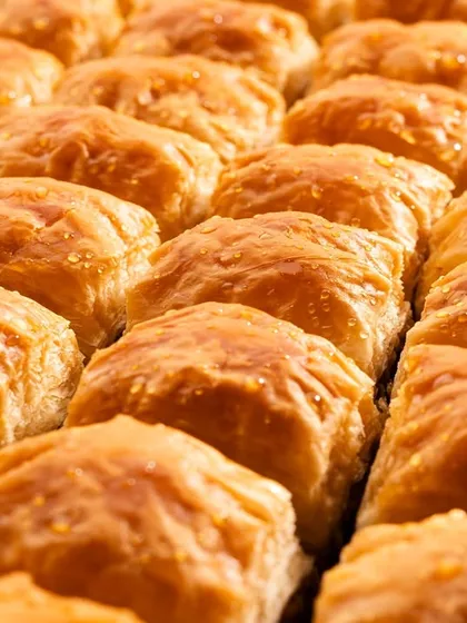 A close-up of classic square baklava, with the light catching the glistening syrup on the golden-brown pastry.