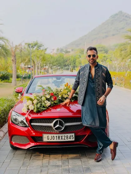 Ready for the baraat, but first, a stylish pose. I always dress to match the event's theme, seen here in a sharp ethnic outfit next to the groom's decorated car.