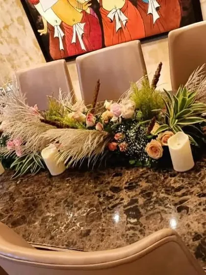 A modern centerpiece for a dinner table, featuring a mix of pink roses, pampas grass, and pillar candles. This style is perfect for creating a warm, rustic, and stylish ambiance.