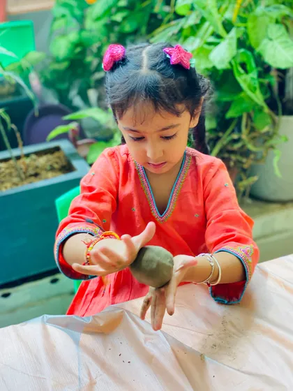 The concentration on her face is priceless! Each child gets to connect with the material at their own pace, feeling the texture of the clay as they create something meaningful.