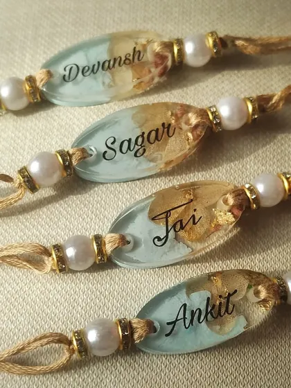 A closer look at the custom name rakhis with a light blue base. The combination of the personalized name, preserved flowers, and gold leaf creates a beautiful keepsake that your brother will cherish.