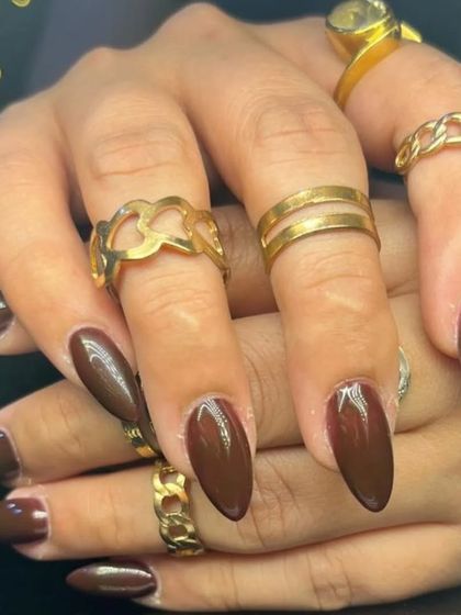 A full set of the rich, dark brown nails, styled with gold rings.