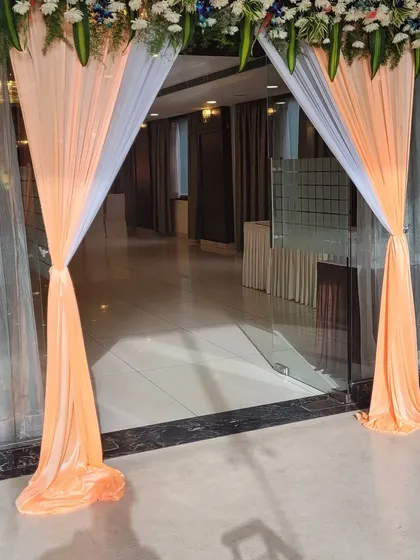 Simple and elegant entrance decor using peach and white drapes tied back to frame the doorway. A floral header adds a touch of freshness, creating a graceful welcome for guests.