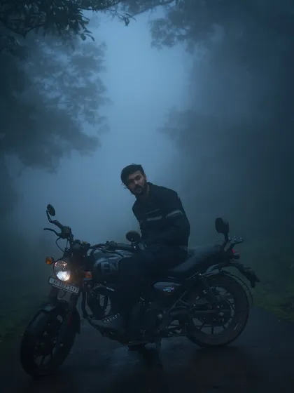 A rider sits on a Royal Enfield Hunter 350, enveloped in dense, blue-toned fog on a remote road. This moody motorcycle portrait captures the quiet solitude and atmosphere of a monsoon ride through the ghats.