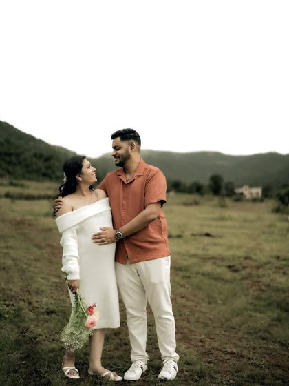 A lovely portrait of the couple standing together in a field. His arm is around her, and they share a look of love and contentment.