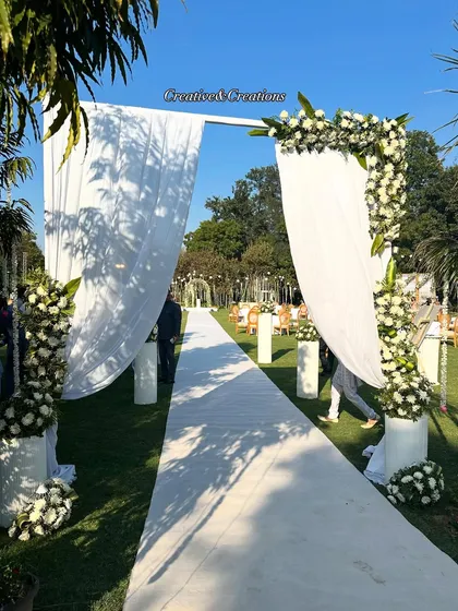 Simplicity at its finest for an outdoor day wedding. This elegant white fabric entrance, adorned with fresh white flowers and greenery, creates a clean and sophisticated pathway for guests on a beautiful lawn.