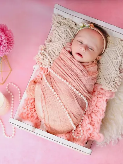 A sweet newborn wrapped in a peach-colored swaddle, sleeping in a tiny bed. The pink background and matching flowers create a warm, monochromatic look.