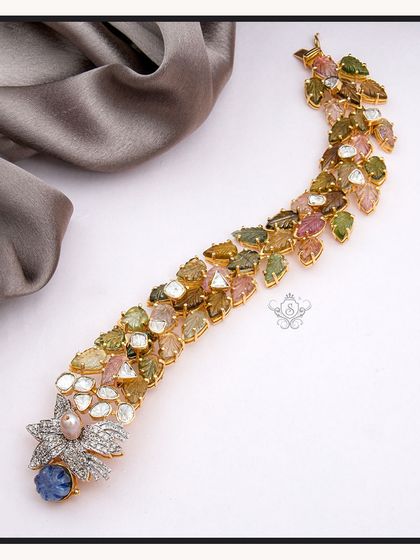 A truly unique piece, this bracelet is crafted with a cascade of multi-colored tourmaline stones and uncut diamonds (polki). The design culminates in a beautiful floral motif with a central blue sapphire, showcasing my expertise in gemstone jewellery.