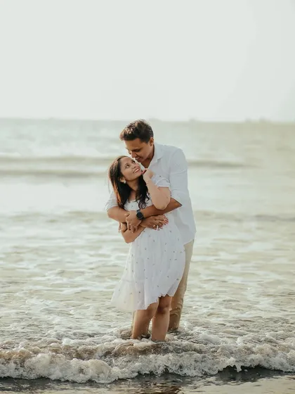 A warm embrace in the ocean waves. This romantic pre-wedding photograph captures a moment of closeness and affection against the vastness of the sea.