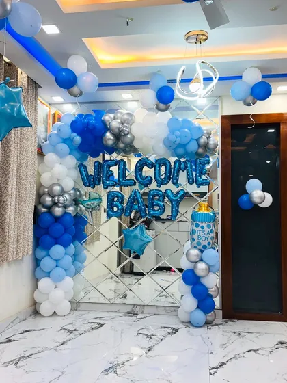Welcoming a new baby is a special occasion, and we decorate your home to make it perfect. This is a 'Welcome Baby' boy setup with a blue and silver balloon arch against a modern mirror wall, creating a clean and celebratory look.