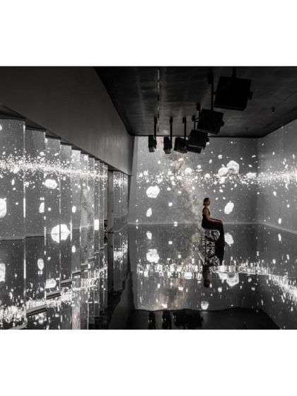 A visitor sits within another immersive installation at the museum, surrounded by projections of a starry cosmos on mirrored surfaces. This space is designed to inspire wonder and self-reflection.