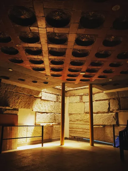 This space features walls made of massive, rough-cut stone blocks and a ceiling constructed with a filler slab technique using clay pots. The dramatic lighting emphasizes the textures and creates an almost cavern-like, ancient feel.