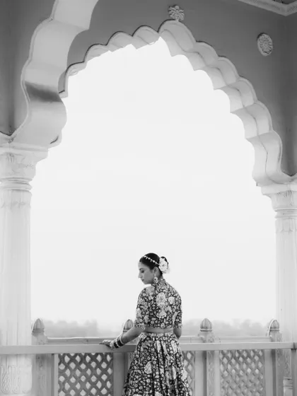 A serene black and white bridal portrait, with the bride framed perfectly by a grand palace archway, creating a clean and classic image.