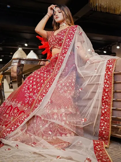 Capturing a moment of grace in a stunning red bridal lehenga. The model's pose and the flow of the sheer dupatta create a sense of timeless beauty, perfect for a brand's lookbook or campaign.