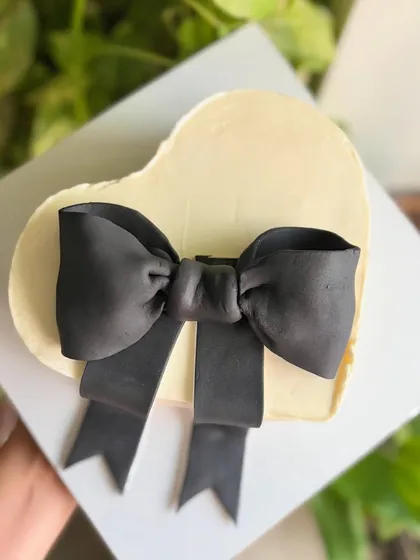 Minimal. Chic. Timeless. A heart-shaped buttercream cake with a dramatic, oversized black fondant bow, perfect for a modern and stylish Valentine's or anniversary gift.