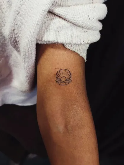 A tiny, single-line seashell with a pearl inside. This delicate tattoo is a beautiful symbol of hidden treasures and inner beauty.