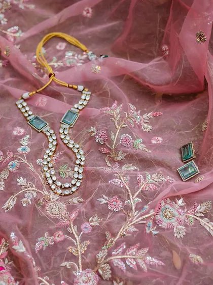 A flat lay of the bride's delicate jewelry set against the intricate embroidery of her pink lehenga.