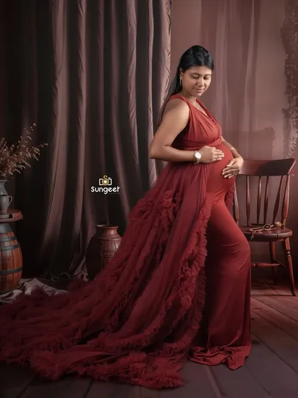 A classic maternity pose in a deep red ruffled gown. The rustic, dark wood background provides a beautiful contrast and a timeless feel.