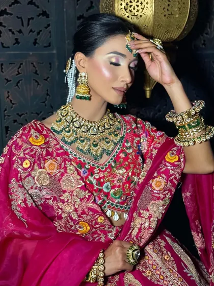 A serene and elegant bridal portrait. The makeup is soft and bronzed, with a focus on contoured cheeks and a neutral lip, letting the heavily embroidered outfit and jewellery stand out.