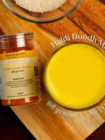 An overhead shot of a glass of Haldi Doodh next to the masala jar and a bowl of sugar. It's a simple, timeless Indian tradition that you can easily recreate at home.